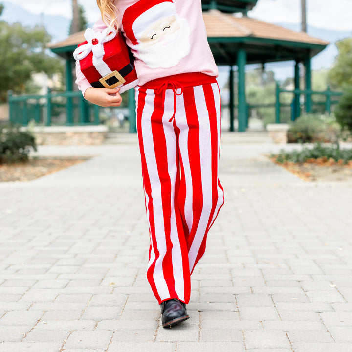 little girl holding Santa gift in red and white striped sweater pants and matching pink Santa sweater