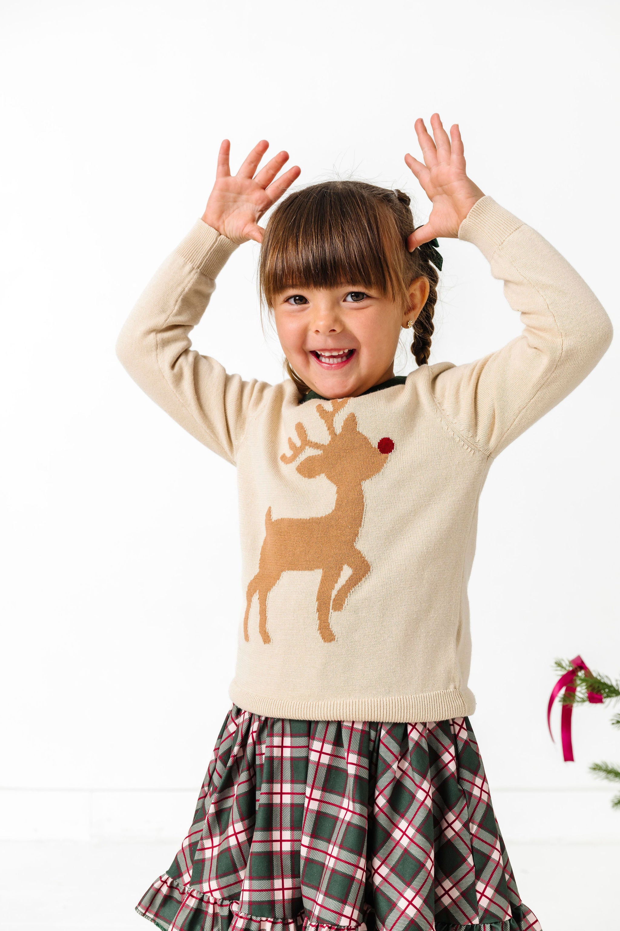 child in cream pullover sweater with red nosed reindeer silhouette design and matching green plaid Christmas dress
