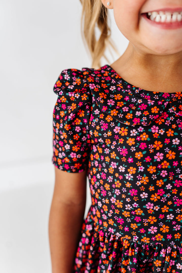 closeup of puffed sleeve and collared dress bodice on little girl wearing black twirl dress with orange and pink flower design