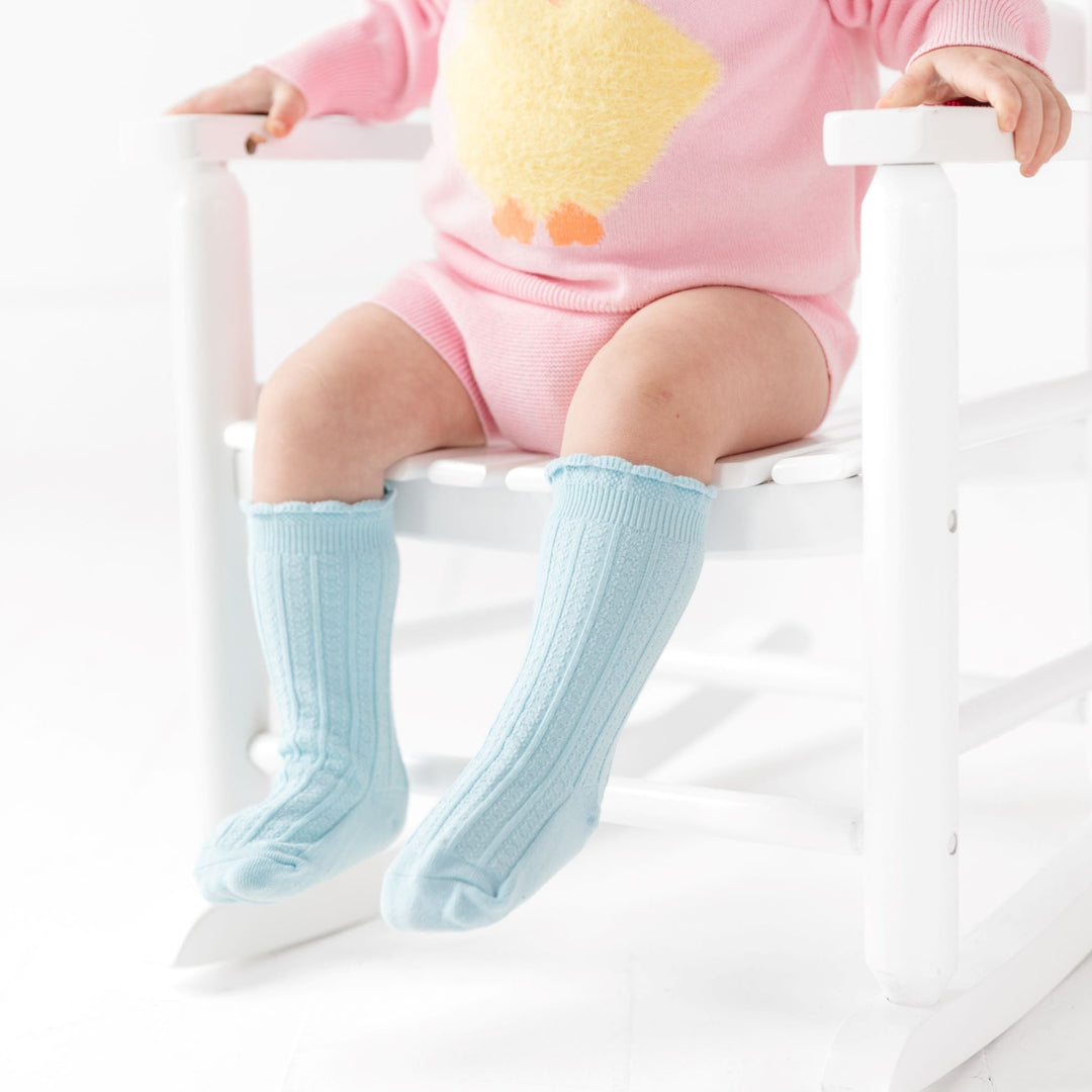 baby girl sitting in pink chick sweater set with robin blue scalloped knee high socks for Easter