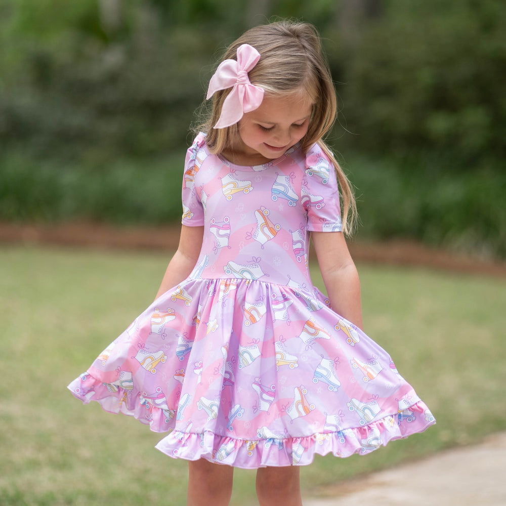 little girl in roller skate twirl dress with hands in pockets and light pink hair bow 
