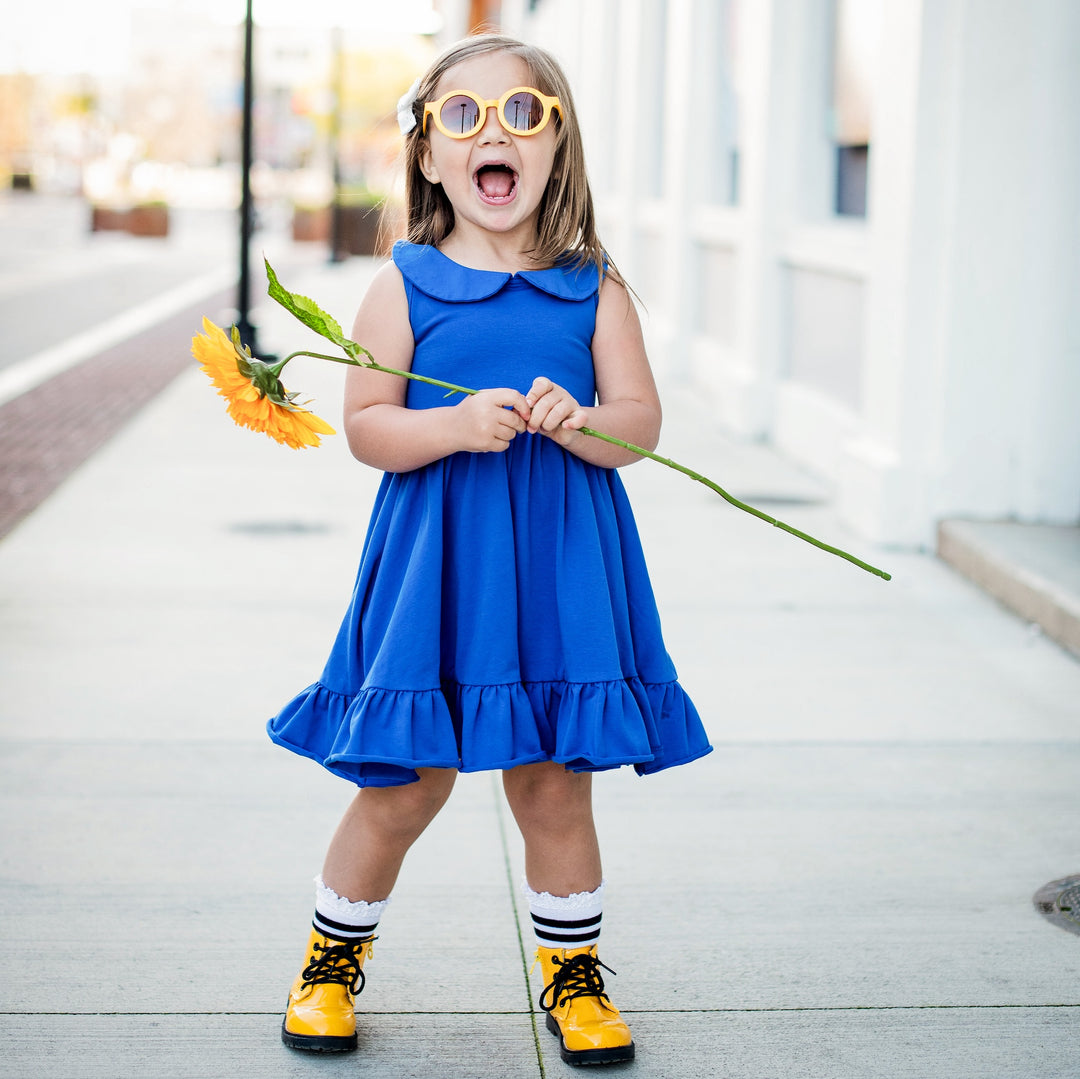 little girl holding sunflower wearing royal blue summer dress and bright yellow sunglasses