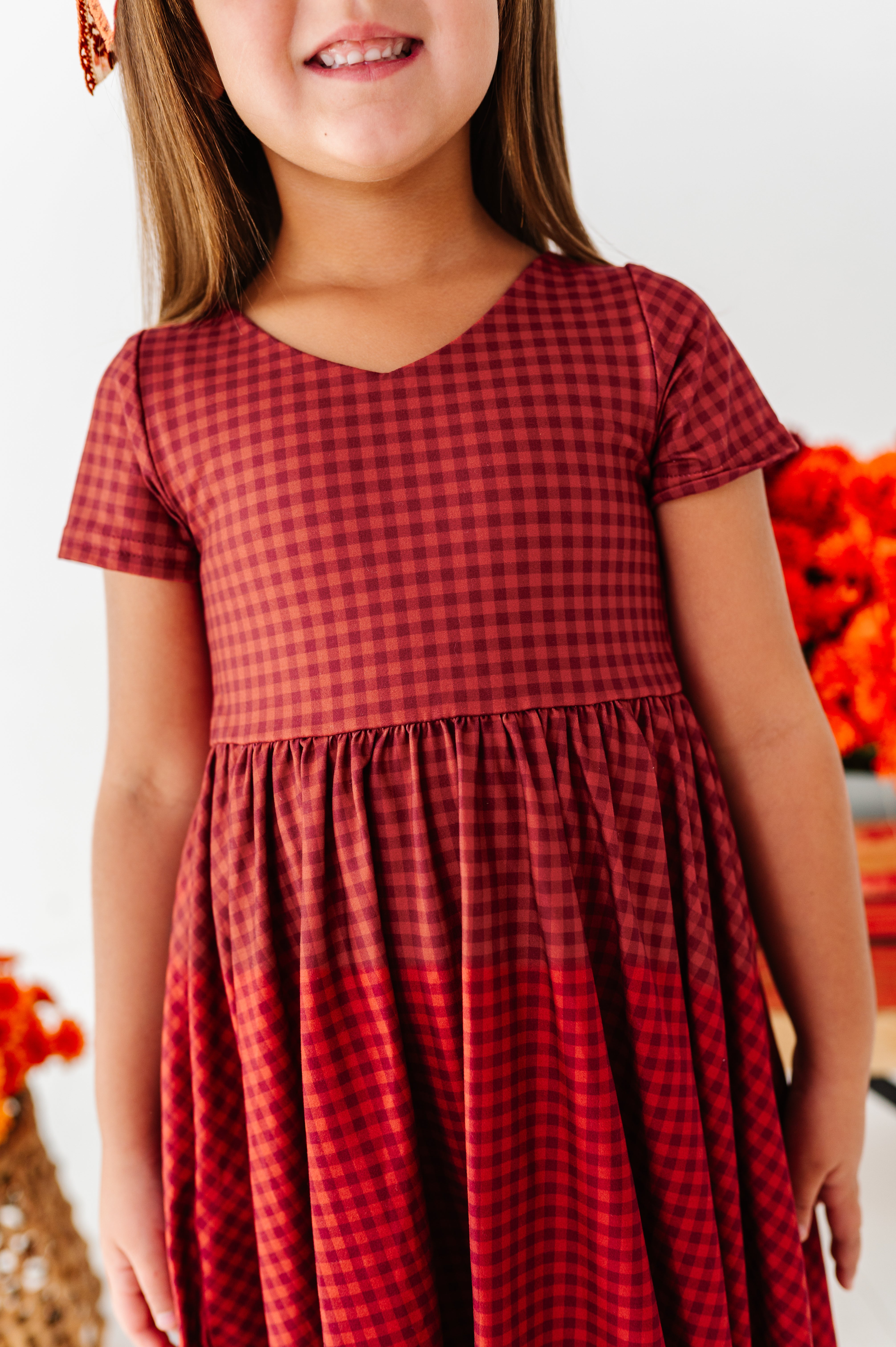 closeup of girl in rust and burgundy dress with orange flowers behind her
