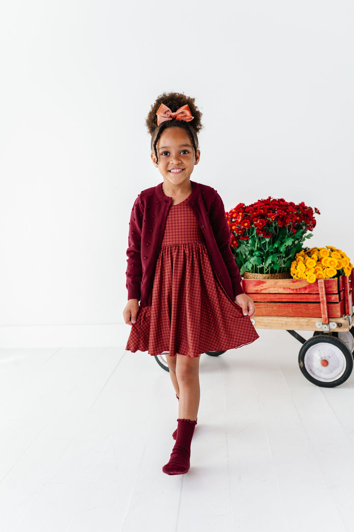 young girl with flower wagon in rust gingham fall twirl dress paired with burgundy cardigan and midi socks and coordinating velvet hair bow