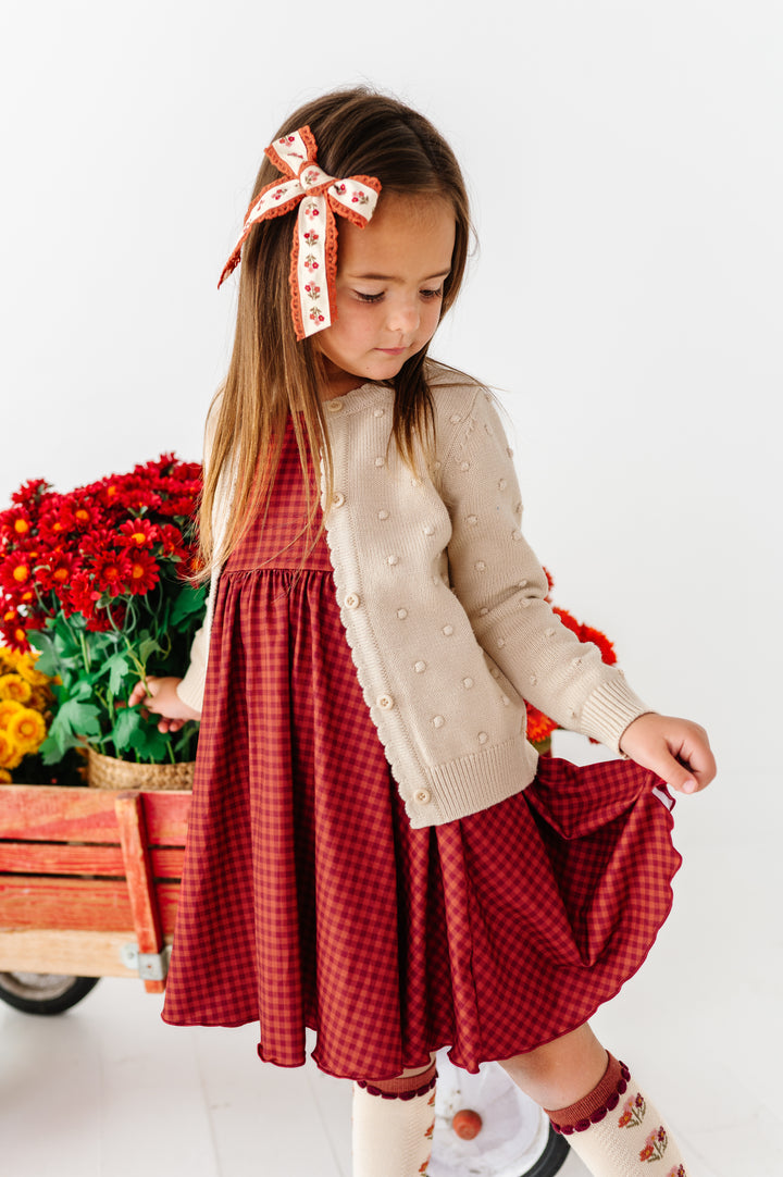 young girl with flower wagon in rust gingham fall twirl dress paired with vanilla cardigan and knee high socks and coordinating printed lace hair bow