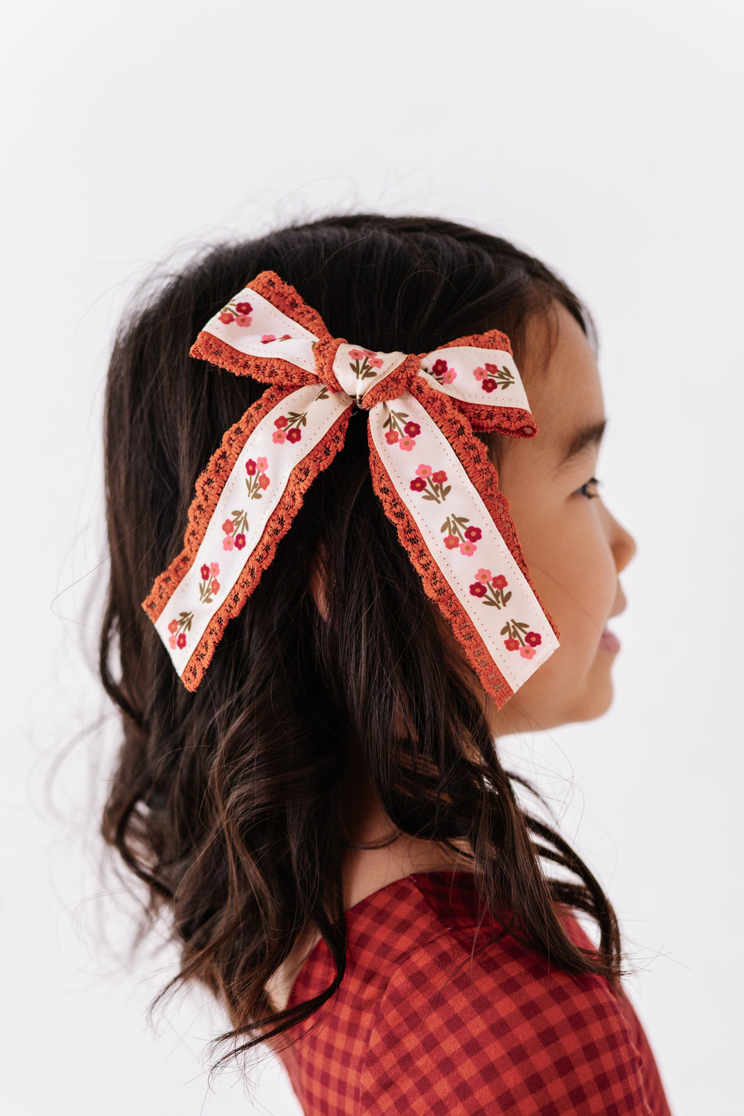 girl wearing fall floral hair bow with matching rust and burgundy gingham 