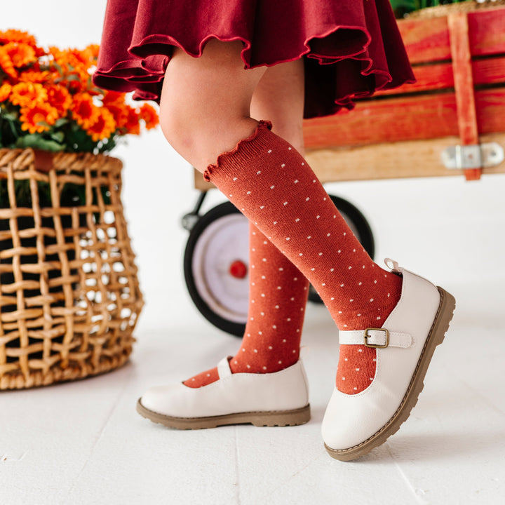 little girl in front of fall decor wearing rust lettuce trim knee socks with cream dots paired with cream mary jane shoes