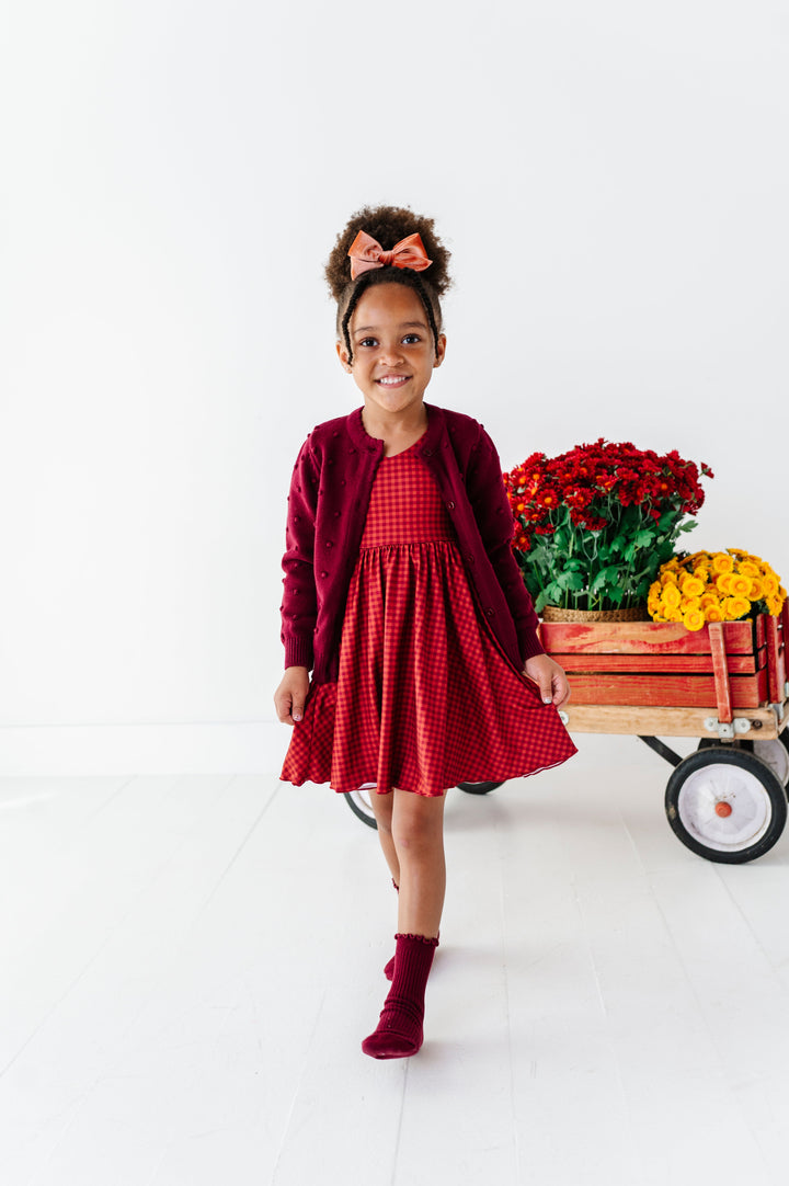 young girl with flower wagon in rust gingham fall twirl dress paired with burgundy cardigan and midi socks and coordinating velvet hair bow