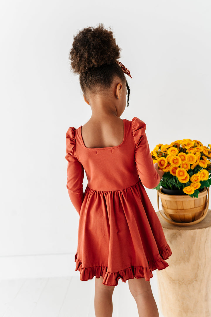 back view of young girl in rust square neck cotton blend long sleeve twirl dress