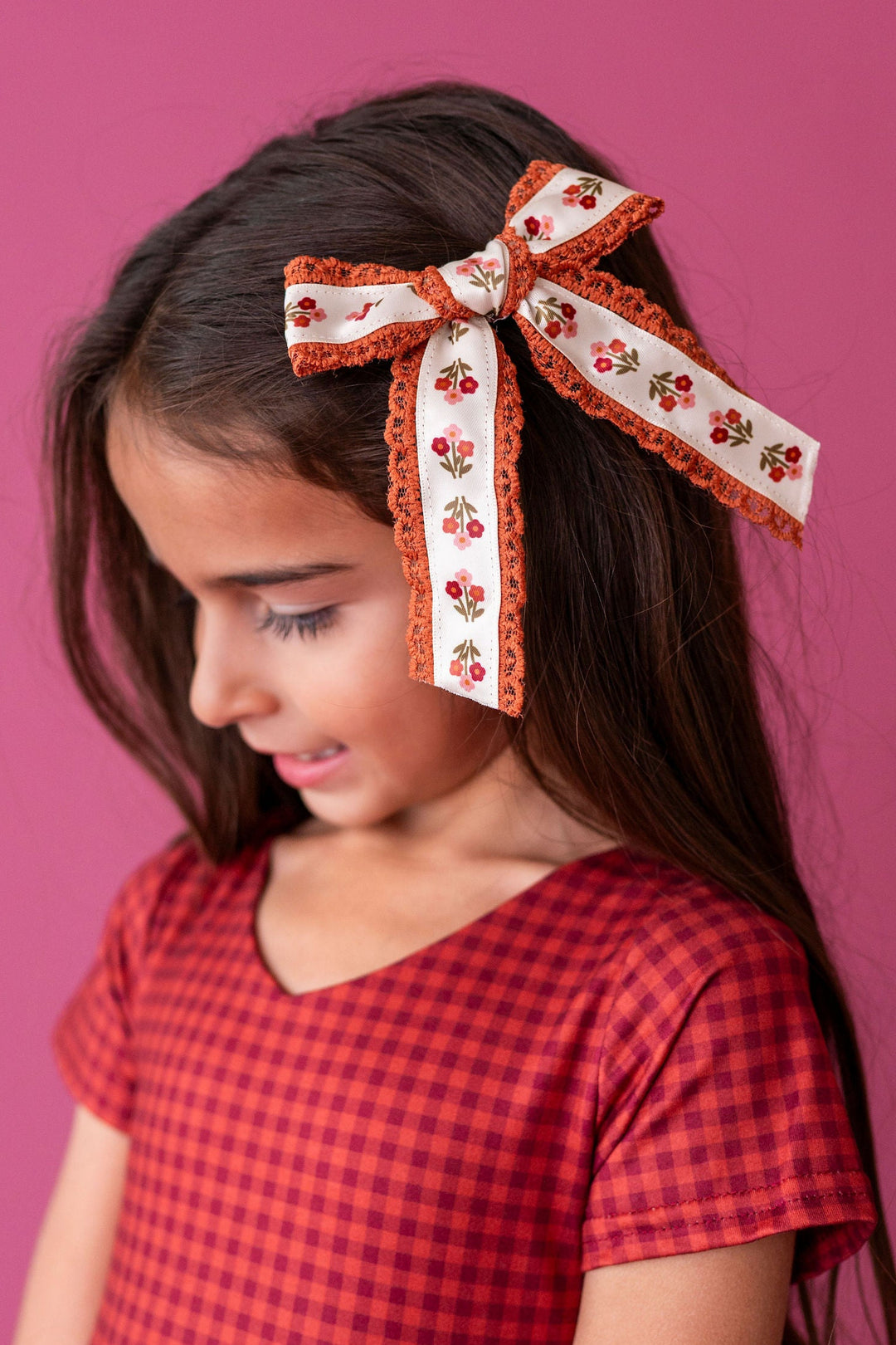 girl wearing fall floral hair bow with matching rust and burgundy gingham dress