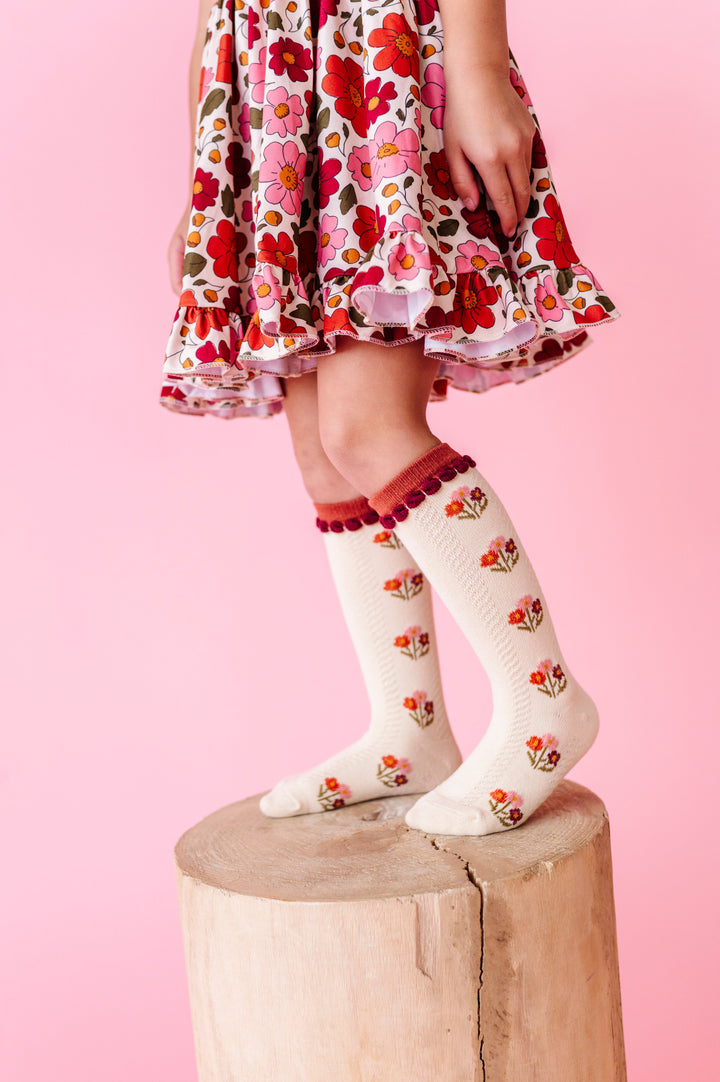 little girl standing on stool in cream knee socks with rust floral design paired with matching rust floral twirl dress