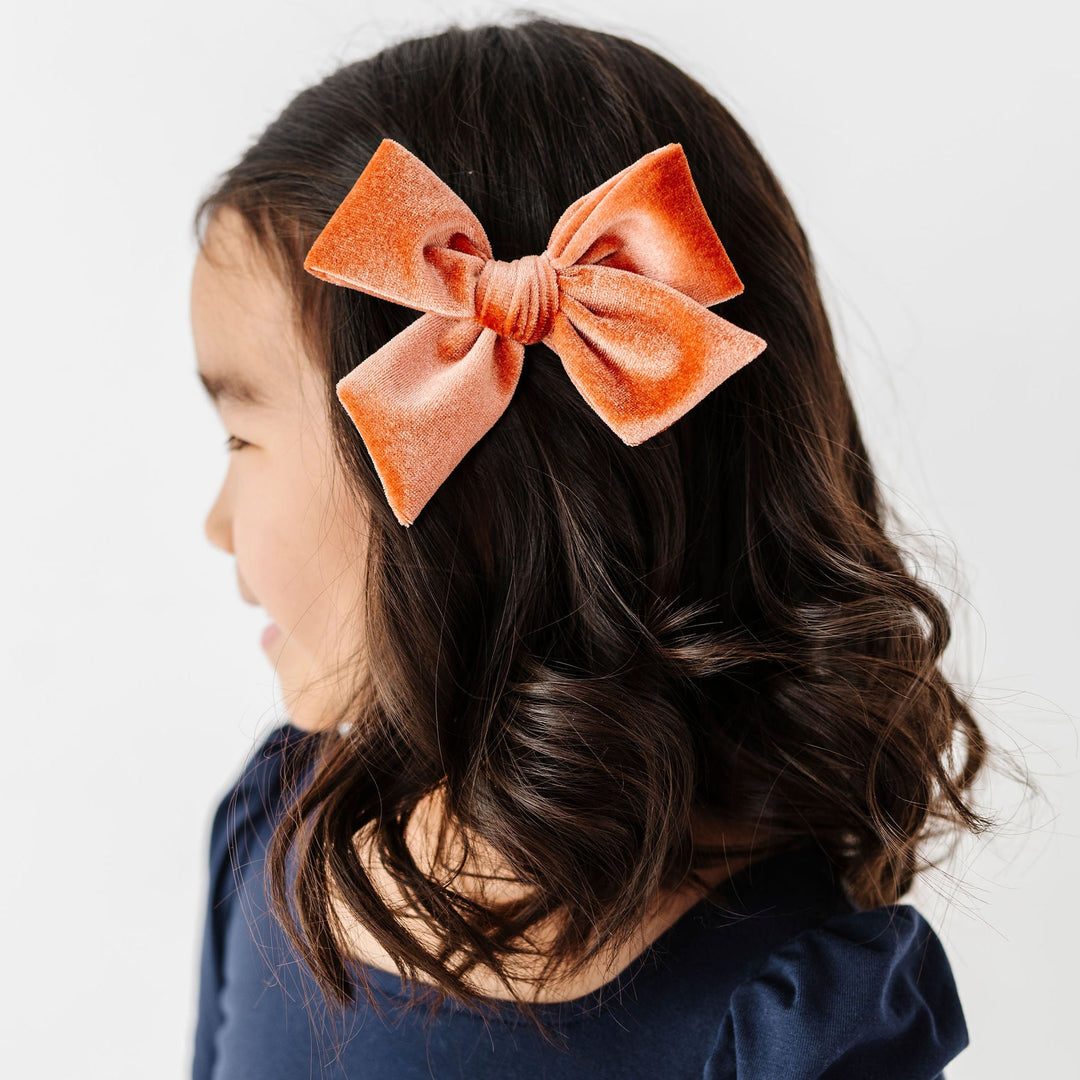 little girl with rust velvet hair bow and navy long sleeve dress