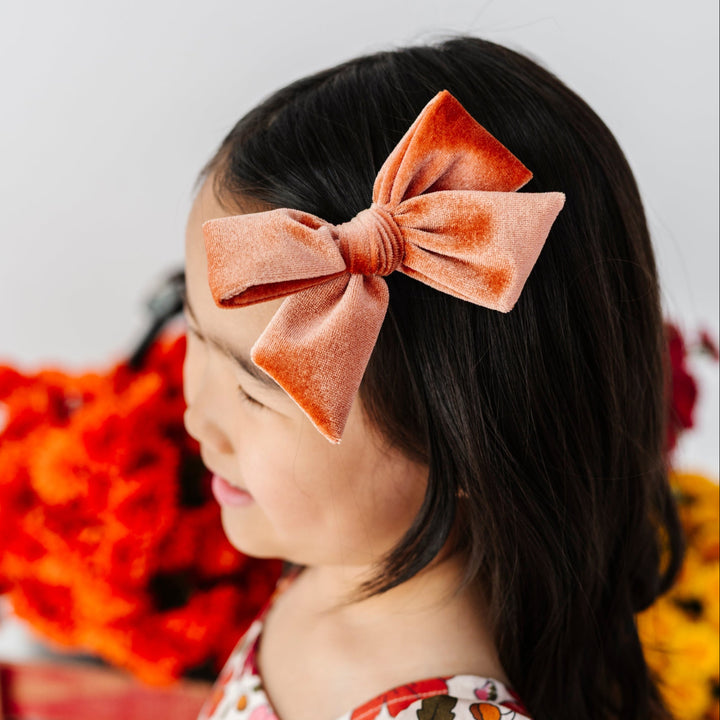 young girl in front of fall flowers wearing rust floral twirl dress paired with rust velvet hair bow on alligator clip
