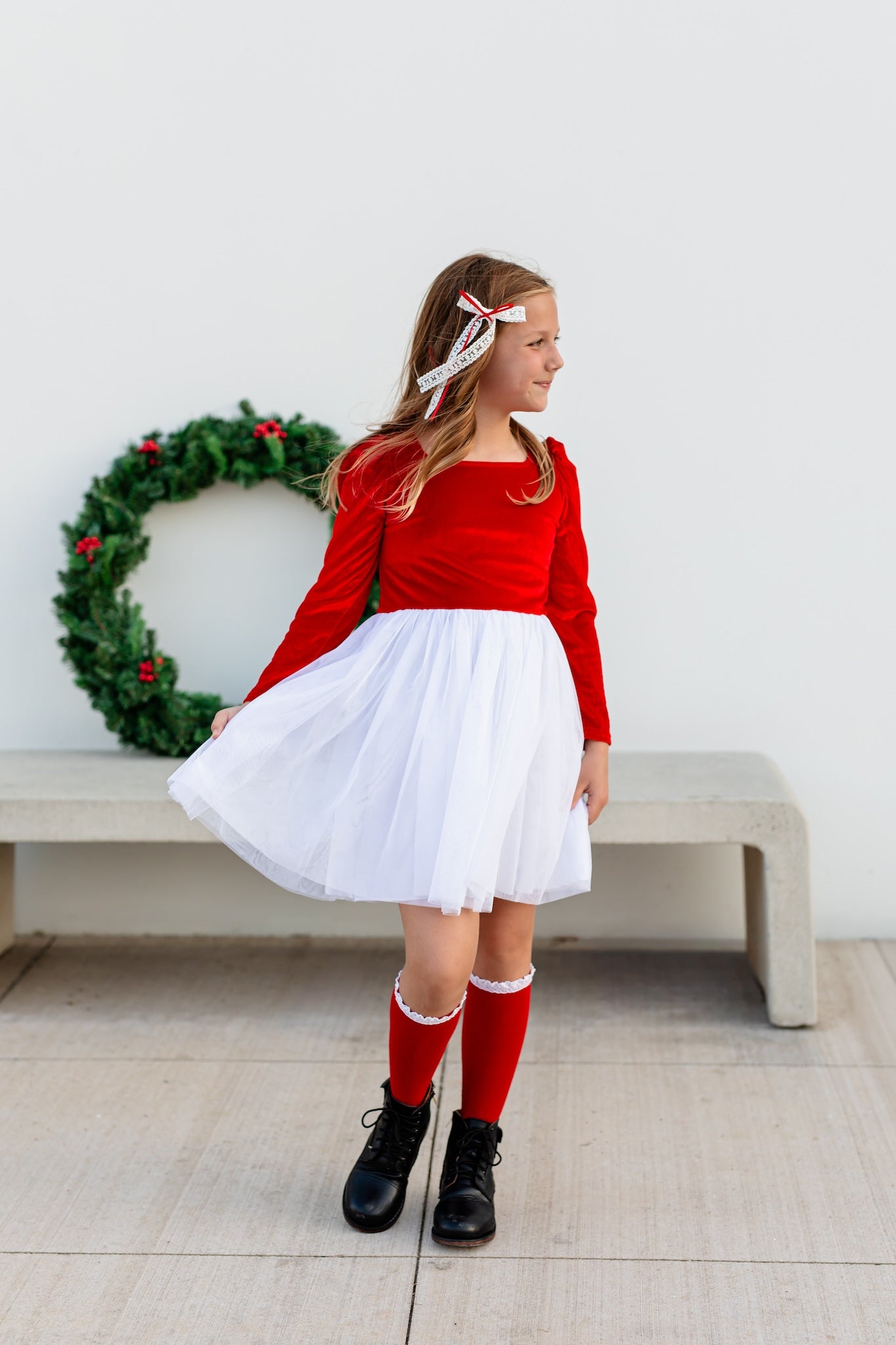 girl in Santa inspired velvet tutu dress with bright red velvet bodice and white tulle skirt paired with red and white knee highs and hair bow
