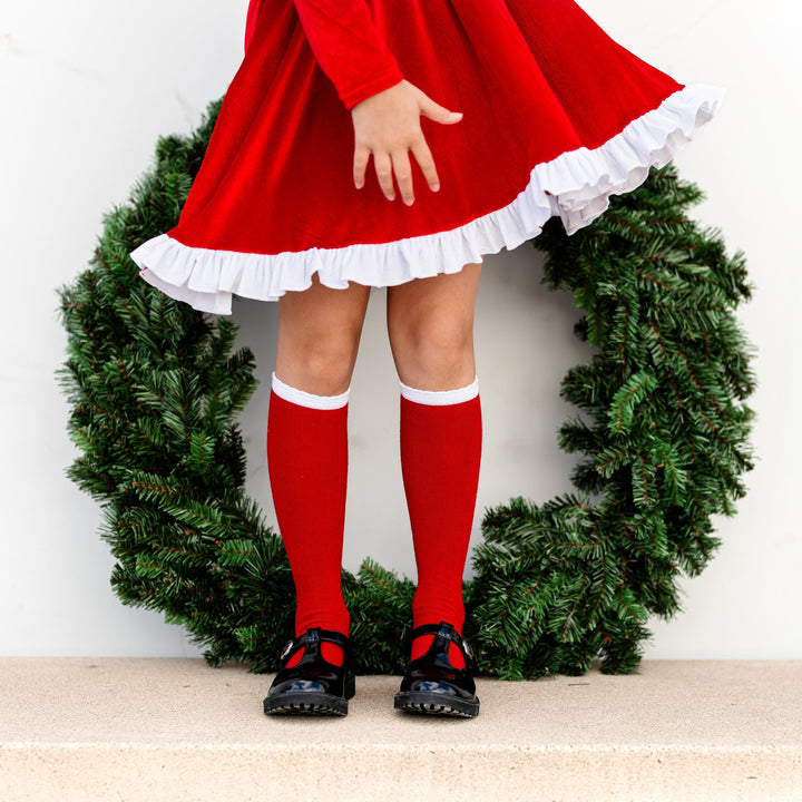 little girl in Santa inspired velvet dress and matching red knee highs with white scalloped border