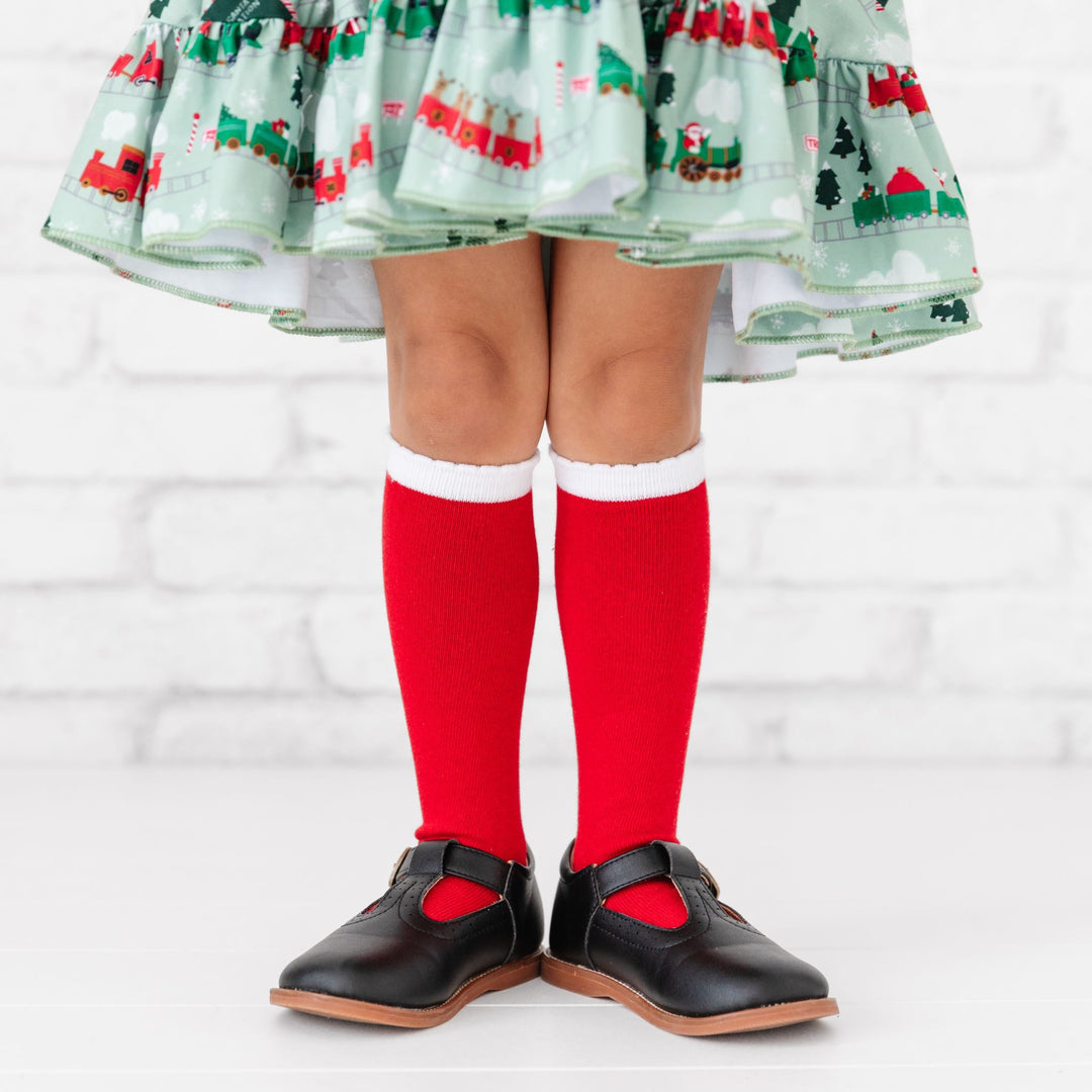 little girl in red knee highs with a white scalloped trim and Christmas train twirl dress