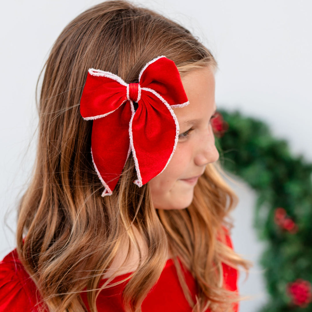little girl in front of Christmas wreath in red velvet hair bow with white velvet trim paired with matching red velvet dress