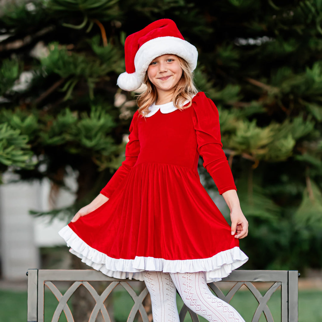 little girl in front of tree in Santa inspired red and white velvet dress and white pointelle tights for Christmas