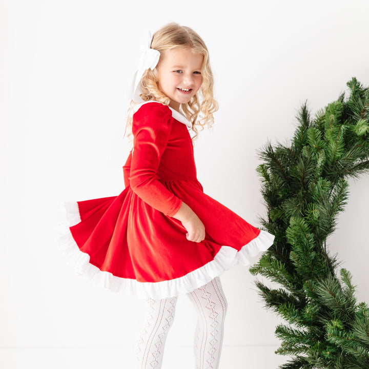 little girl twirling in red and white velvet santa dress, white satin bow and white open knit tights