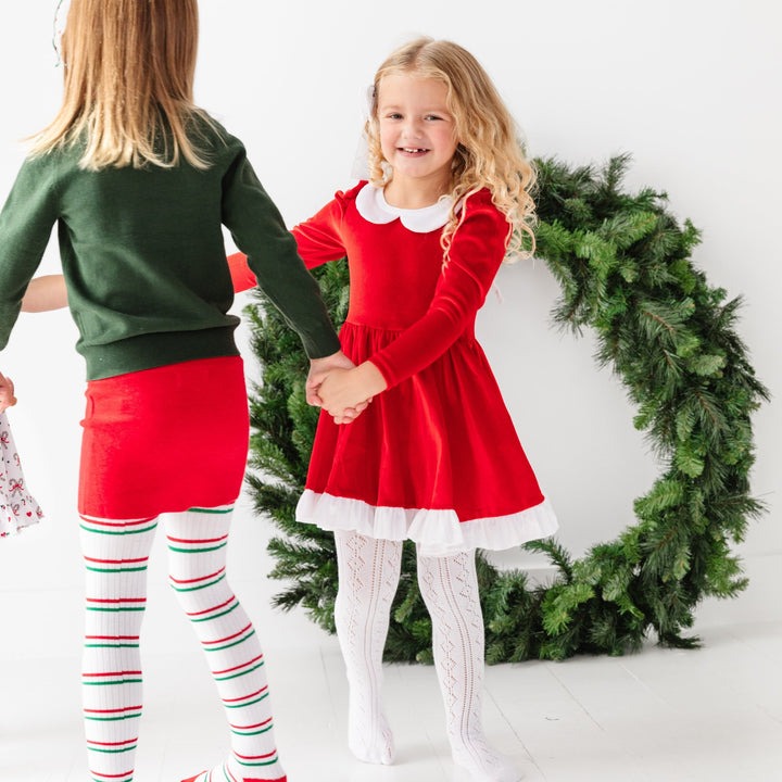 little girl in Santa inspired red velvet twirl dress with white trim and white open knit tights for Christmas