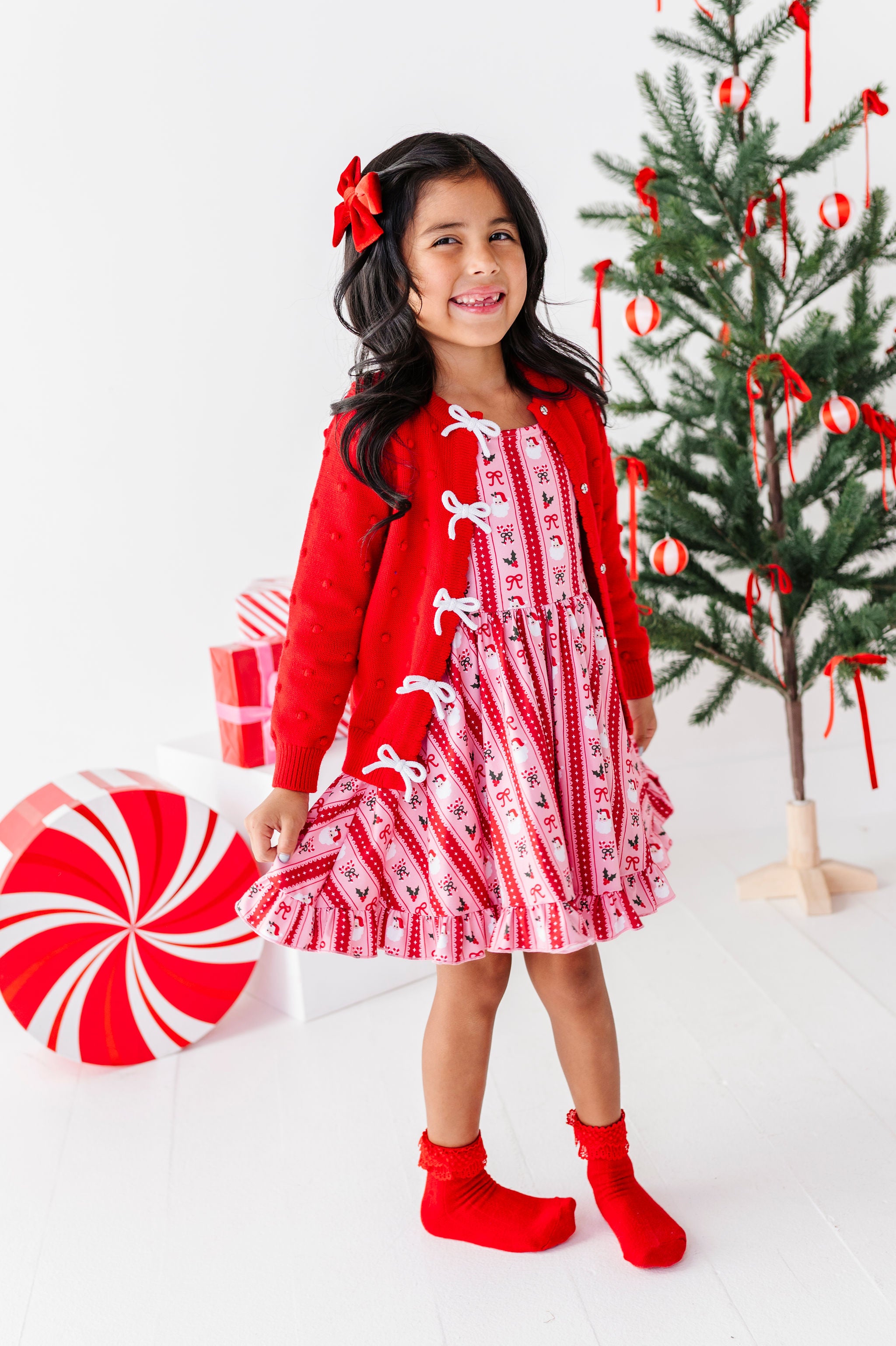 girl wearing pink and red santa wallpaper print dress with matching red and white bow cardigan