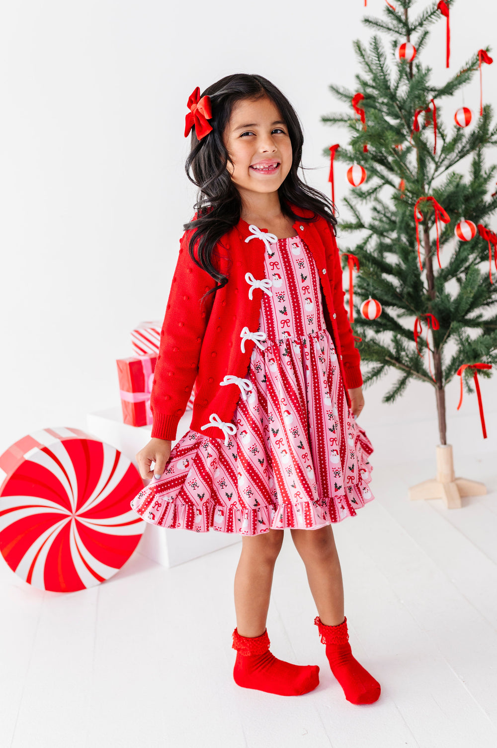 girl wearing pink and red santa wallpaper print dress with matching red and white bow cardigan