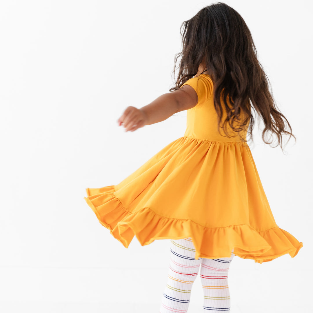 little girl twirling in school bus yellow cotton pocket dress and rainbow striped tights