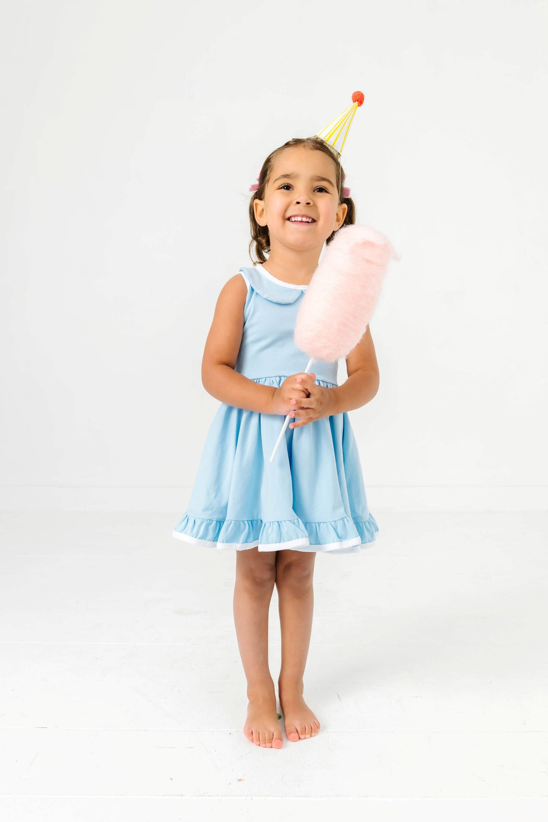little girl holding cotton candy and wearing party hat in light blue twirl dress with white trim and peter pan collar