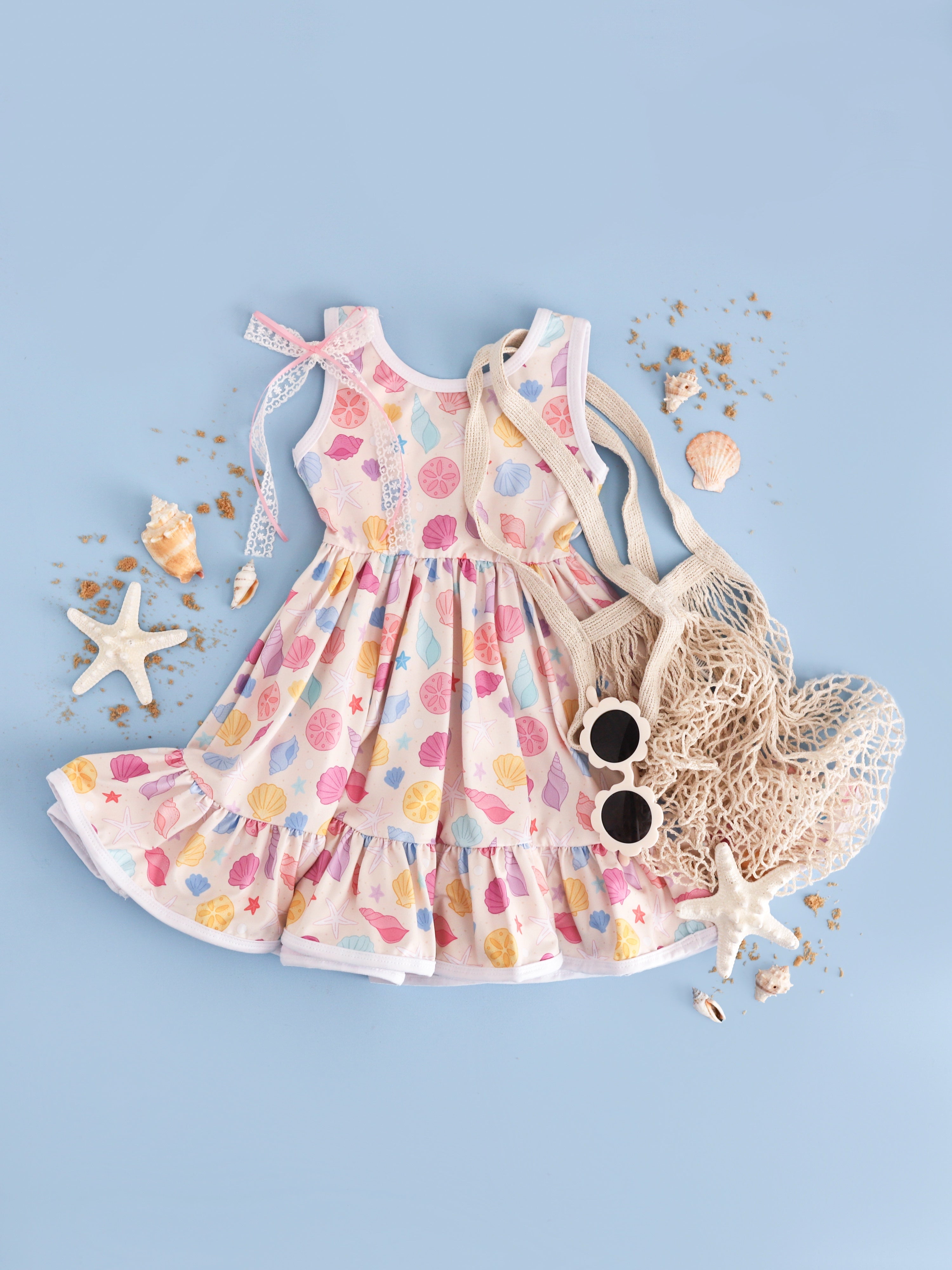 girl's sleeveless seashell print twirl dress styled with seashells and beach accessories 