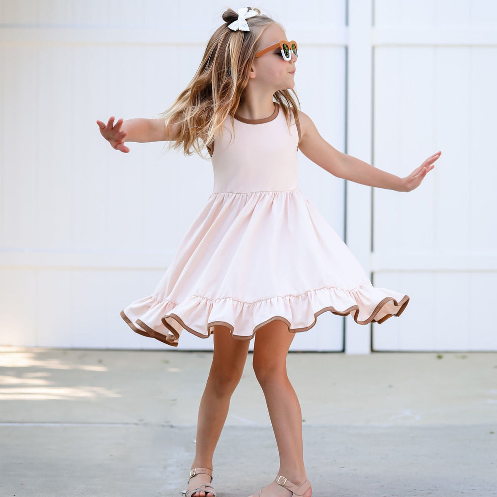 girl twirling in cream dress with taupe trim