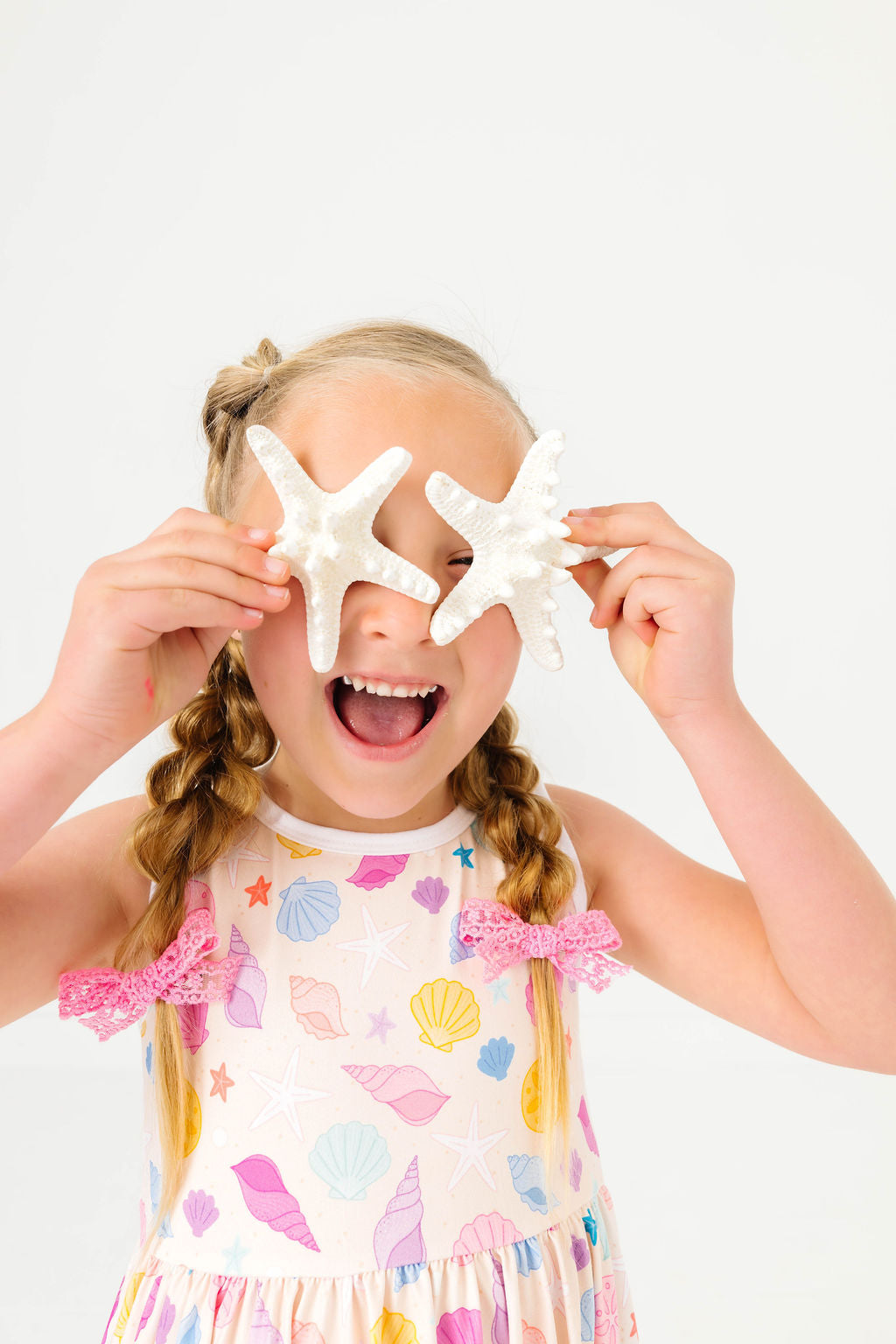 little girl holding starfish in seashell print summer twirl dress and pink lace pigtail bows