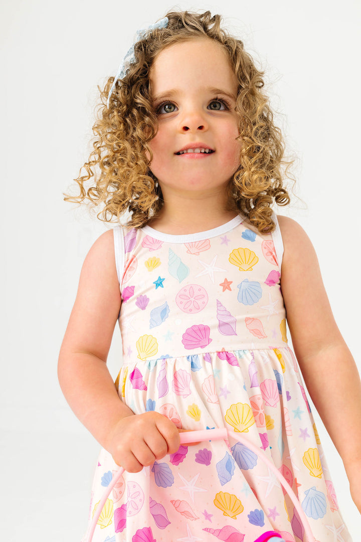 little girl in sandy cream-colored twirl dress with colorful seashell print and white trim for summer
