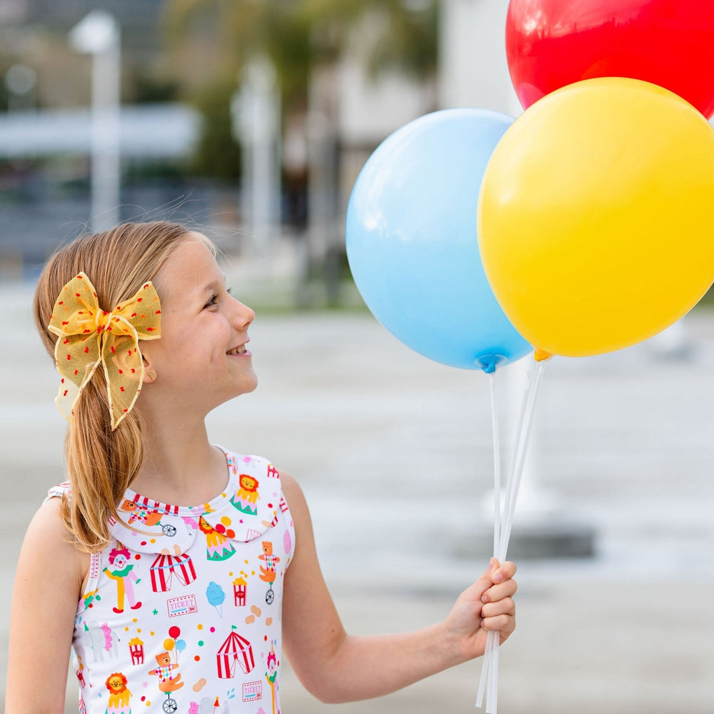 yellow and red circus inspired hair bow on little girl wearing circus dress and holding balloons