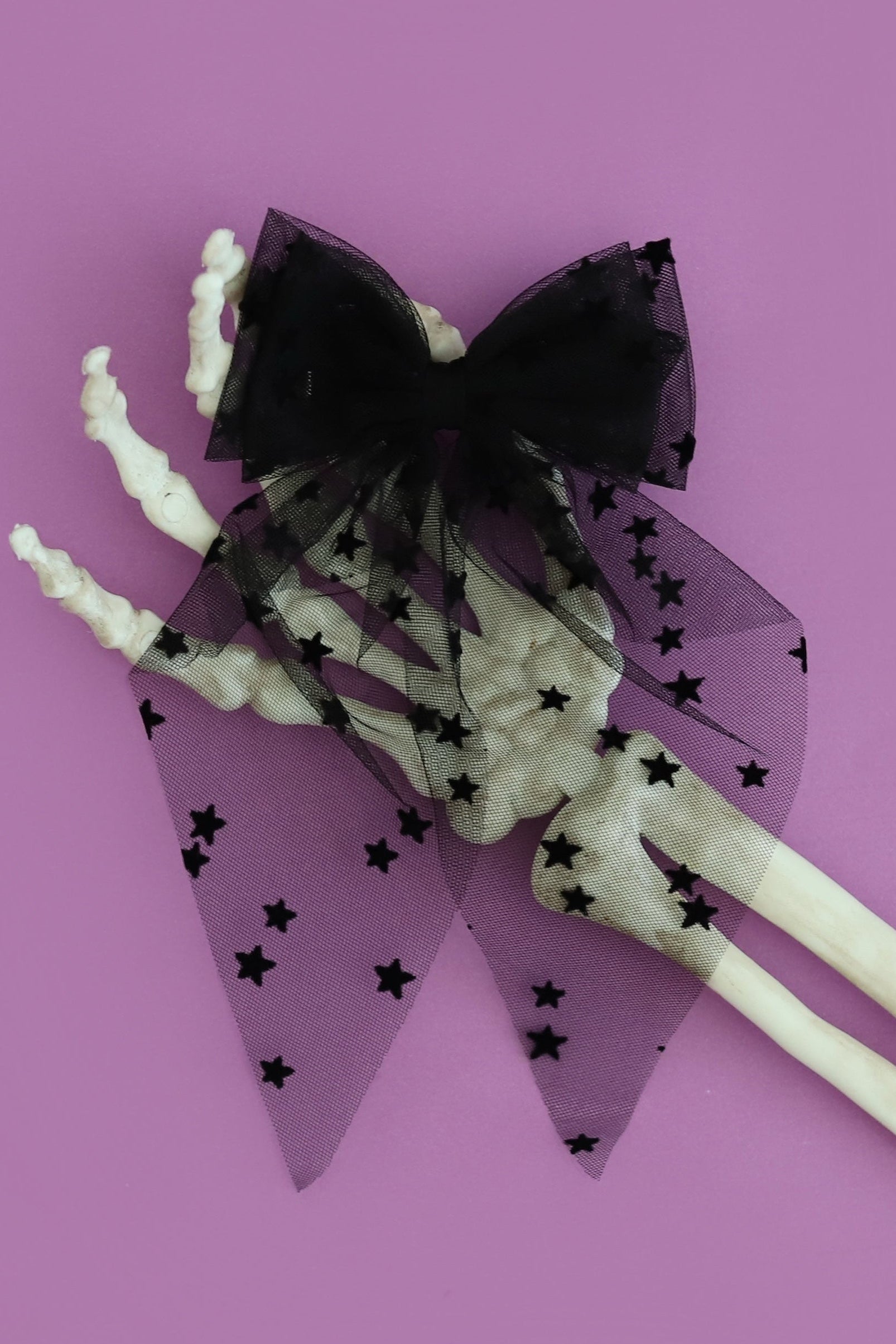 girls sheer black tulle hair bow on clip with tiny velvet stars photographed on purple background with skeleton hand
