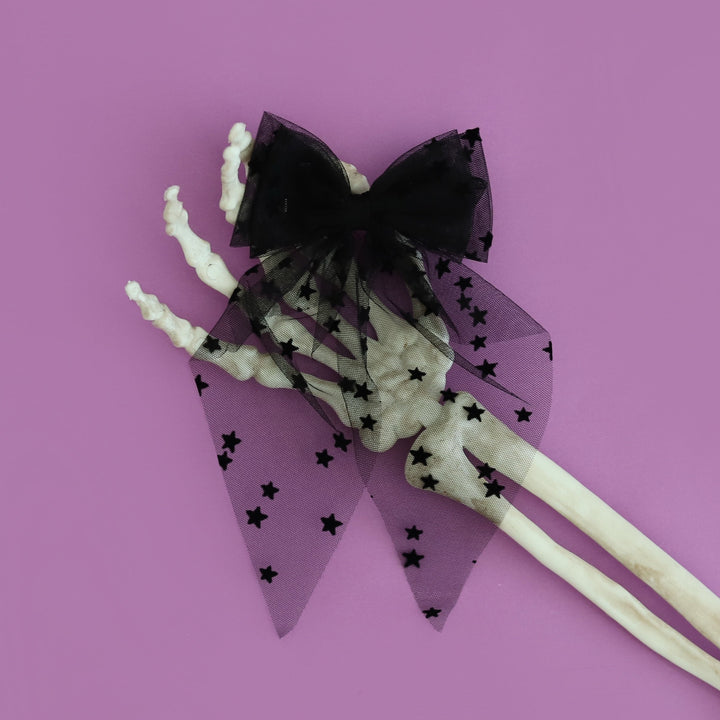girls sheer black tulle hair bow on clip with tiny velvet stars photographed on purple background with skeleton hand