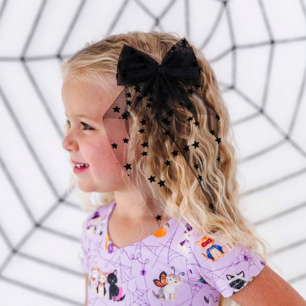 young girl in purple Halloween kitten twirl dress paired with sheer black hair bow with tiny star embellishments and spiderweb backdrop