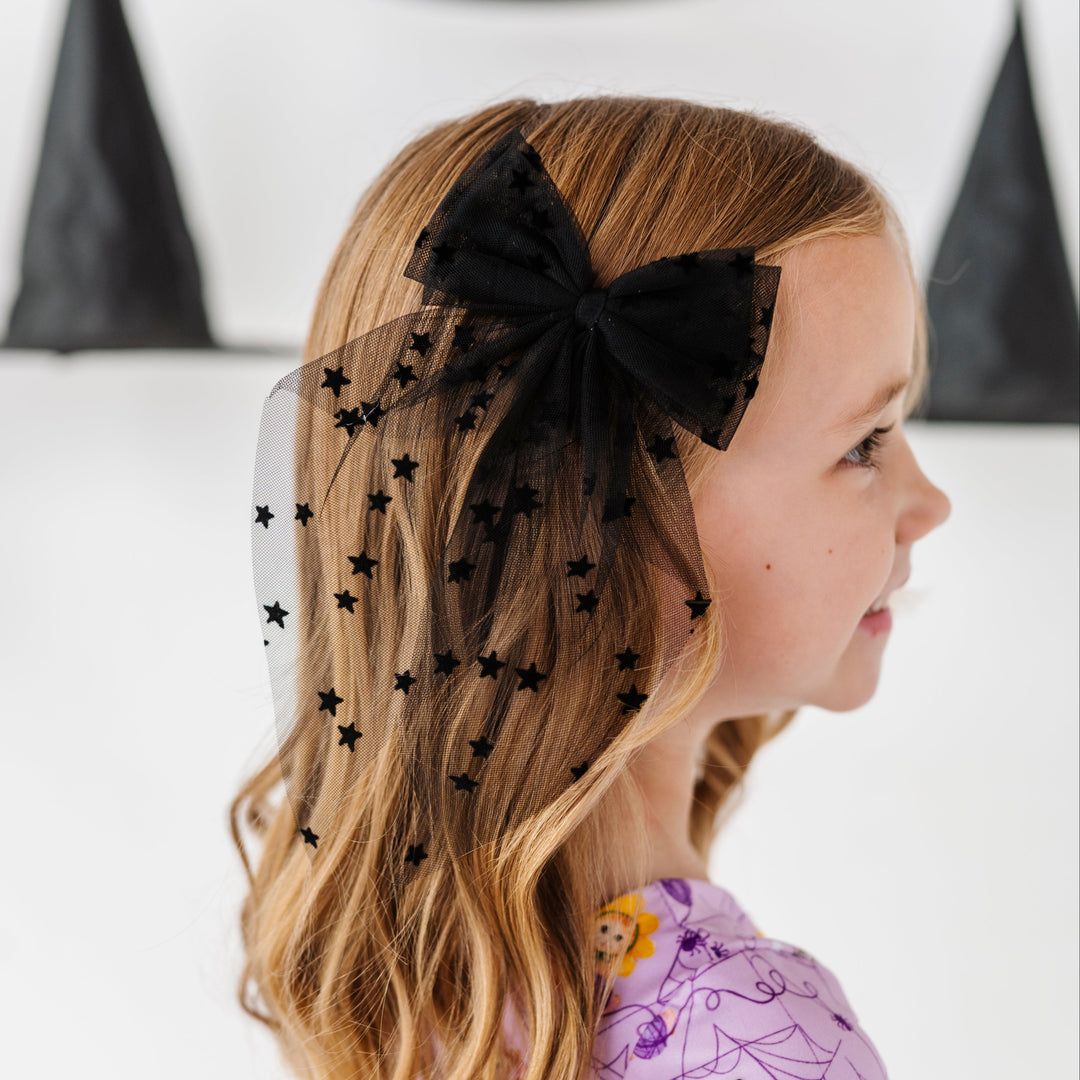 young girl surrounded by witches hats wearing black tulle hair bow with small velvet star design paired with purple Halloween kitten print twirl dress