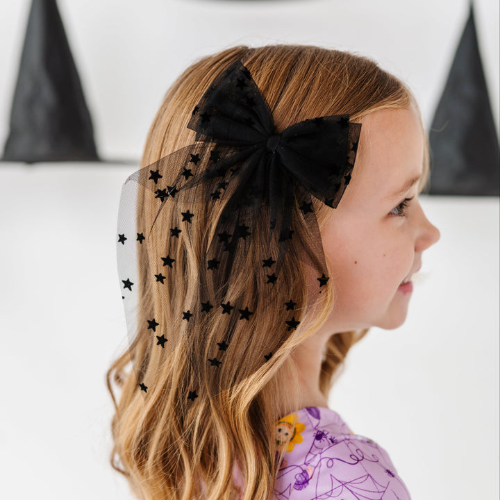 young girl surrounded by witches hats wearing black tulle hair bow with small velvet star design paired with purple Halloween kitten print twirl dress