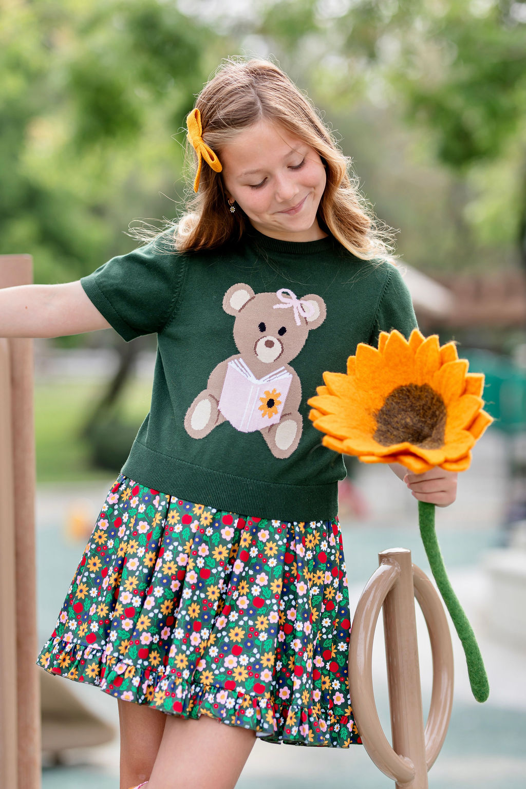 girl holding sunflower in short sleeve green sweater top with bear design and forest green floral and apple print twirl dress