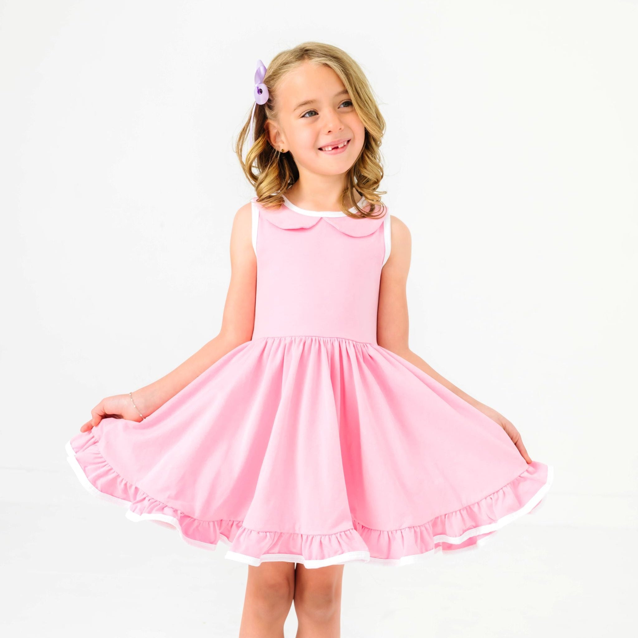 little girl in cotton candy pink twirl dress with peter pan collar and white trim paired with lavender satin hair bow
