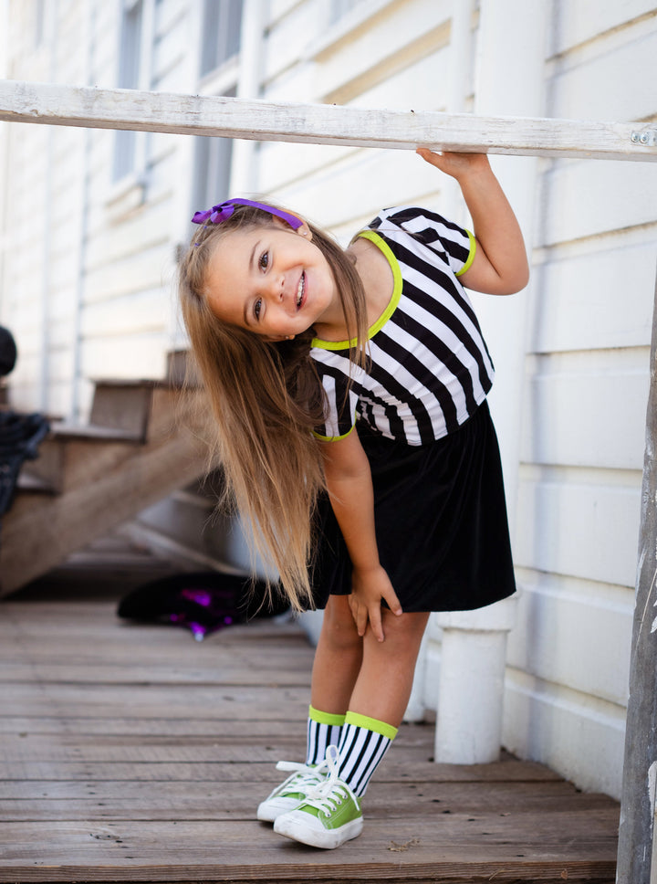 little girl in Beetlejuice inspired black and white striped top, black velvet skort and matching striped midi socks with green sparkle trim