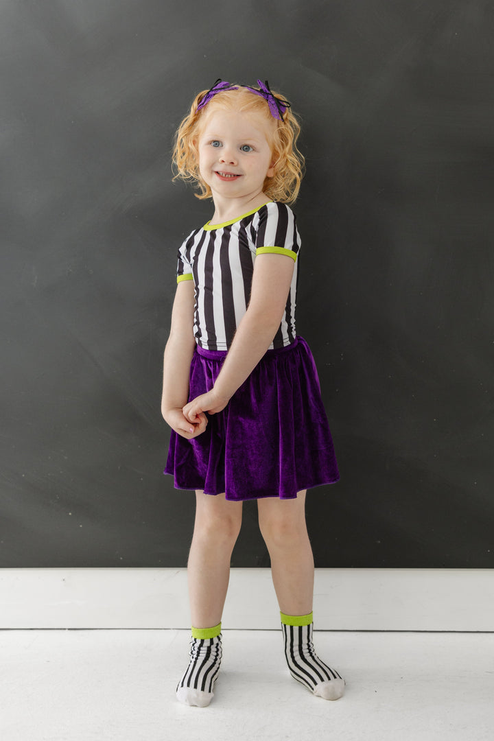 little girl in Beetlejuice inspired black and white stripe top and midi socks with green trim paired with purple velvet skort for Halloween season