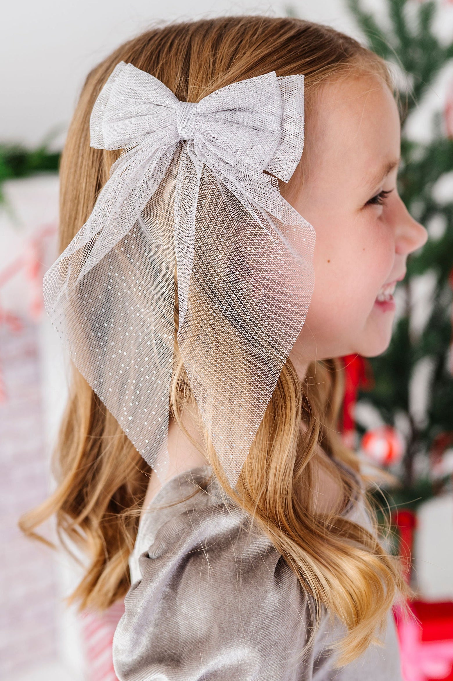 profile of little girl wearing a sparkly silver tulle hair bow with a blurred holiday background