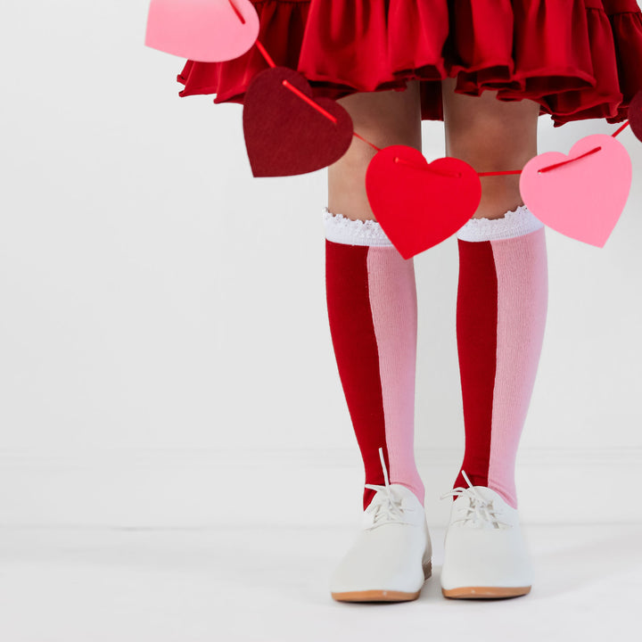 girl standing holding heart garland and wearing red and pink colorblock knee high socks for valentines day
