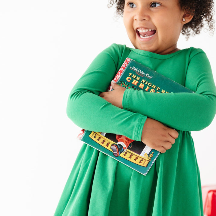 little girl holding holiday book in bright Christmasy green cotton dress with long sleeves