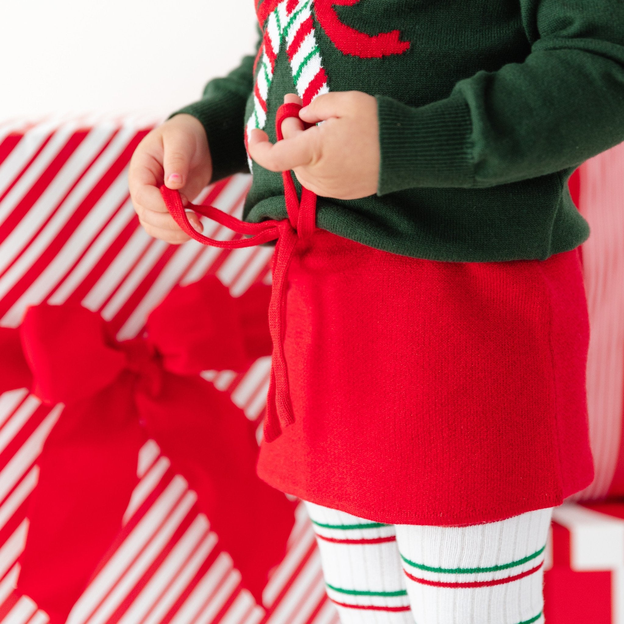 little girl in bright red sparkly sweater skirt, matching candy cane sweater and striped Christmas tights