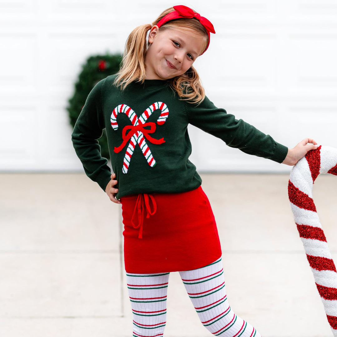 little girl in candy cane knit sweater, Christmas striped tights and matching red sweater skirt with drawstring