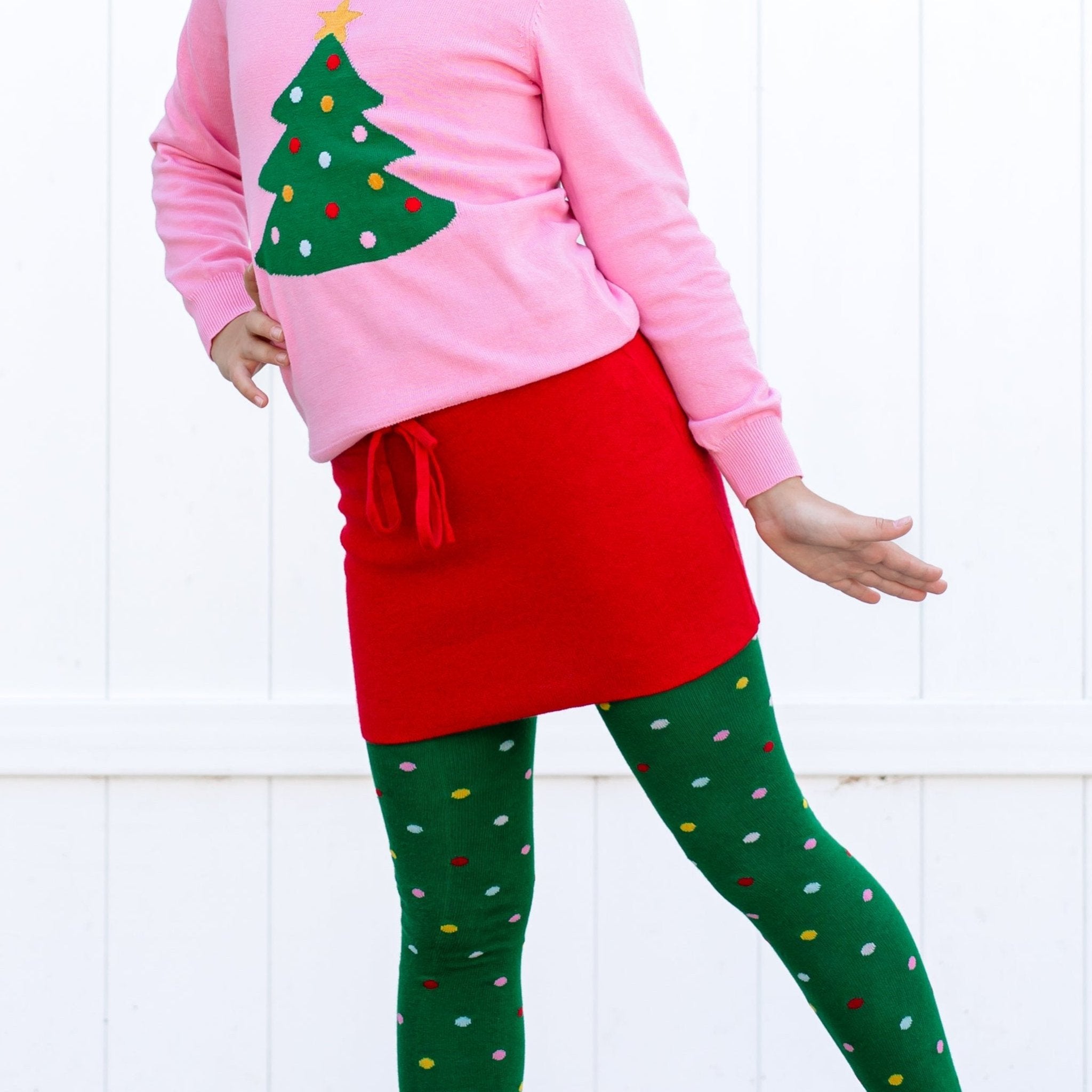 little girl in sparkly bright red knit sweater skirt with drawstring, green tights with multicolored dots and matching tree sweater