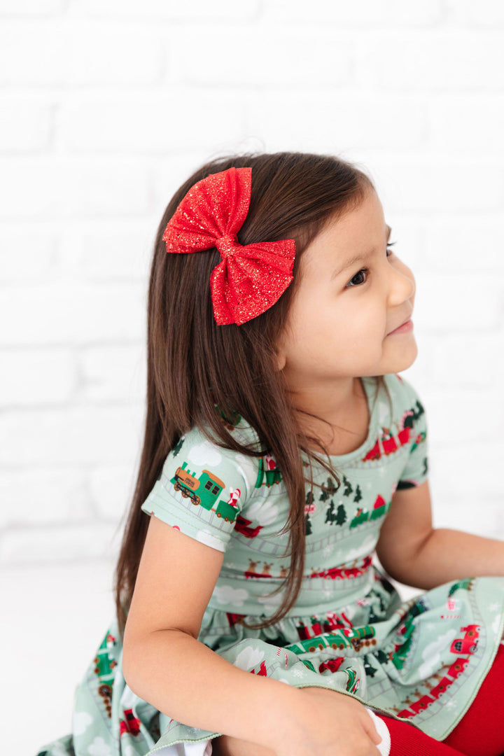 little girl wearing sparkly red hair bow to match christmas train dress