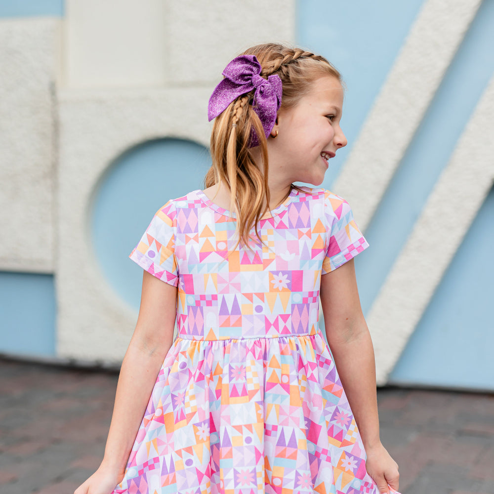 little girl wearing small world inspired dress with matching sparkly purple hair bow